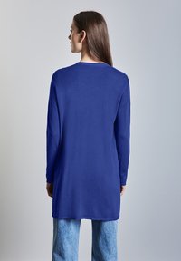 Långärmad tröja i enhetlig blått stickad material, med en avslappnad passform och rund halsringning, i kombination med ljusblå vida jeans.