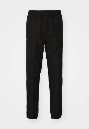 Svarte treningbukser med elastisk midje, smale ben og en liten logo detalj på siden. Glatt tekstur og lett materiale.