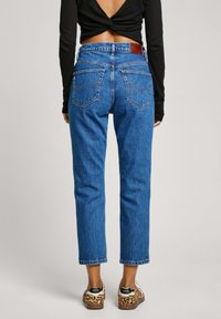 Farkut, joissa on korkea vyötärö, kapeat lahkeet ja vaaleansininen väri. Edessä ja takana taskut sekä nahkainen merkki vyötäröllä.