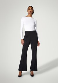 Vit långärmad topp i kombination med högmidjade svarta utsvängda byxor, som har en elegant design och subtila sömdetaljer. Svarta klackar fulländar looken.