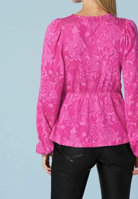 Top peplum floral rosa con mangas largas abullonadas, tejido texturizado y cintura ajustada. Combinado con pantalones negros ajustados.