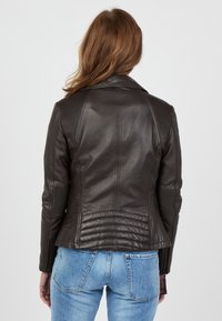 Tumma ruskea nahkamoottoripyörätakki, jossa on pystysuorat poimintakoristeet harteilla ja hihoissa. Takissa on muotoiltu malli ja vetskareilla varustetut hihansuut.