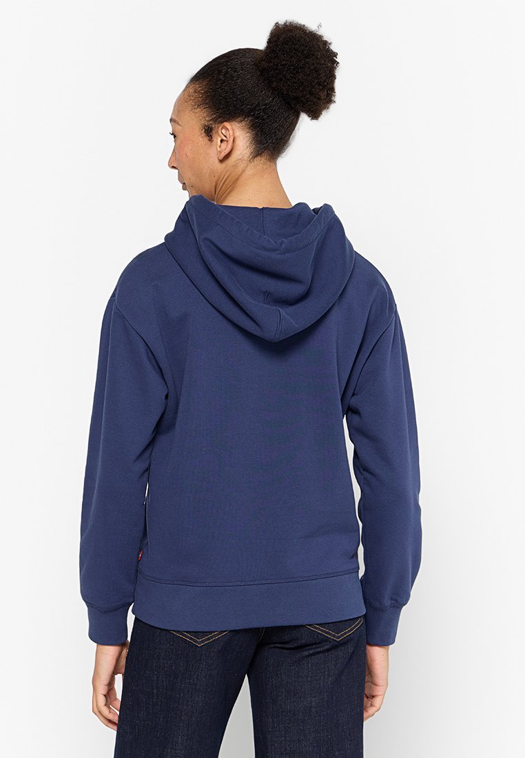 Sudadera con capucha de color azul marino hecha de tejido suave, con un bolsillo tipo canguro, puños acanalados y un corte holgado, mostrando una vista trasera sencilla.