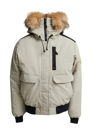 Beige winterjas met een afneembare bruine bontcapuchon, zwarte accenten, twee zijzakken, een ritszak op de borst en elastische manchetten.