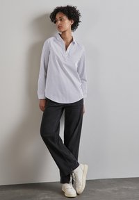 Skjorta med långa ärmar och krage i vertikala ljusa och mörka ränder, parat med vida svarta jeans och vita sneakers. Slät, avslappnad textur.