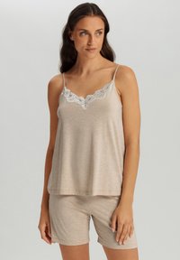 Conjunto de pijama beige con una camiseta sin mangas con borde de encaje y pantalones cortos a juego. La tela parece suave con una sutil textura. Diseño simple y relajado.