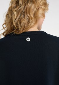 T-shirt in cotone blu navy con scollatura rotonda e un piccolo dettaglio a bottone bianco sulla parte superiore della schiena. Tessuto morbido e a coste.