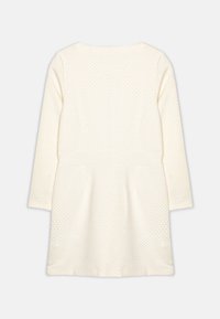 Sukienka z długim rękawem w kolorze kremowym, z fakturowanym wzorem w wypukłe kropki. Okrągły dekolt i rozkloszowany krój spódnicy. Gładki materiał.