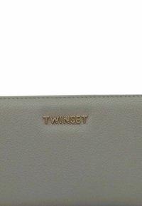 Portafoglio in pelle grigia chiara con una texture liscia, caratterizzato dal logo dorato "TWINSET" sulla parte anteriore e da una cucitura pulita lungo i bordi.