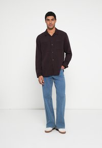 Sötét lila, gombos ing két mellzsebbel, világoskék, bő szárú farmerrel és fehér, barna talpú tornacipővel párosítva.