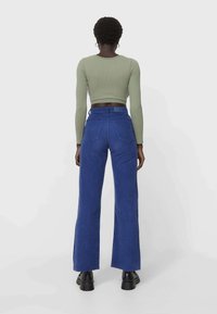 Blaue Cord-Flared-Hosen mit hoher Taille und Gesäßtaschen, kombiniert mit einem taillierten, olivgrünen, gerippten Langarmoberteil.