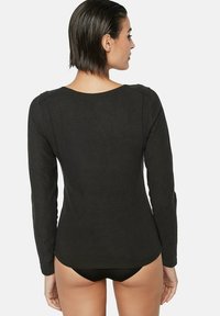 Chemise noire à manches longues en matière douce avec un col rond et des détails de coutures, ajustée à la taille, ouverte au dos.