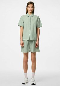 Camicetta a maniche corte a righe verdi e bianche abbinata a pantaloni corti coordinati, con chiusura a bottoni e tessuto dalla texture particolare.