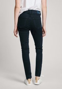 Slim-fit tmavě modré džíny s zadními kapsami, mírným vyblednutím a logem na pase. V kombinaci s bílými teniskami.