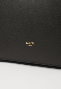 Fekete bőr pénztárca sima textúrával, középen, az alján egy aranyozott bélyegzett "Lancel Paris" logóval.