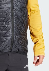 Schwarze, gesteppten Weste mit strukturierter Oberfläche, kombiniert mit einem gelben Langarmoberteil. Verfügt über einen Reißverschluss und überlappende Stofflagen.