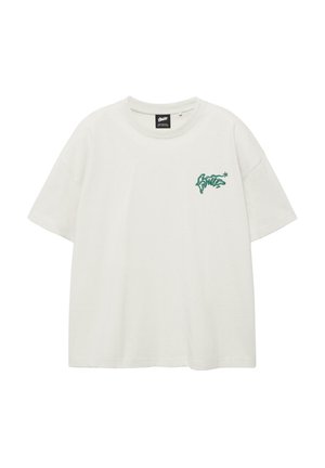 Fehér, oversized, rövid ujjú póló zöld graffiti stílusú felirattal a bal mellrészen, apró csillag részlettel.