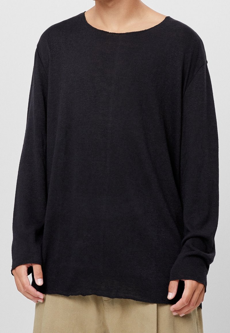 Czarna koszula z długim rękawem, szerokim dekoltem i luźnym krojem, wykonana z lekkiego materiału; posiada surowe wykończenie na dole i opadające ramiona.