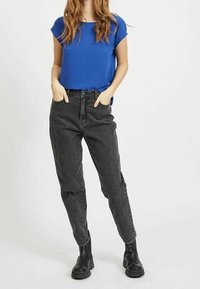 Blå kortärmad topp kombinerad med högmidjade svarta denimjeans och svarta ankle boots. Jeans med tapered passform och lätt blekta områden.