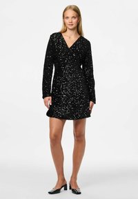 Vestido mini negro con lentejuelas, escote en V profundo y mangas largas. Presenta una cintura ajustada y un dobladillo acampanado. Textura suave y detalles brillantes.