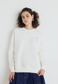 Witte sweatshirt van zachte katoen, met een klein roze grafisch logo op de linkerborst en ribgebreide manchetten bij de mouwen en onderkant.