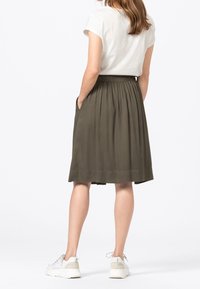 Olivově zelená, sukně s délkou po kolena, s nařaseným elastickým pasem a postranními kapsami; v kombinaci se jednoduchým bílým tričkem s krátkým rukávem.