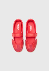 Red Adidas shoes featuring a combination of smooth and suede textures, with a Velcro strap and white accents on the sides.