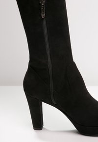 Czarna wysoka kowbojska botka, wykonana z zamszu, z bocznym zamkiem błyskawicznym, lekko spiczastym noskiem i solidnym słupkowym obcasem. Gładka tekstura i elegancki design.