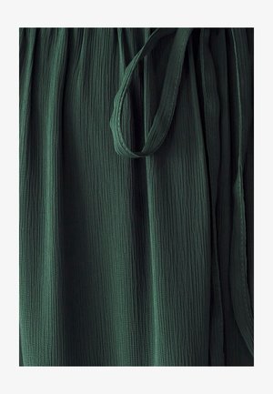 Grøn tekstureret stof med lodrette folder og en bundet talje. Materialet forekommer let og luftigt, hvilket forbedrer dets fald.