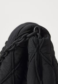 Black padded bag with a textured surface, featuring a chain handle and diagonal stitching details. The material appears soft and smooth.