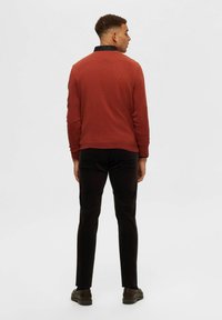 Rostfärgad långärmad skjorta med svart krage, kombinerad med svarta byxor och bruna skor. Slät textur, ledig passform, inga synliga mönster.