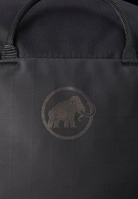 Svart teksturert bag med to solide svarte håndtak og en matt svart logo av et mammut i en sirkulær ramme på forsiden.