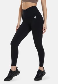 Höga svarta leggings gjorda av stretchigt material, med en subtil logotyp på vänstra låret och en slät, matt yta.