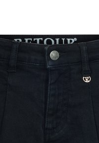 Donkerdenim jeans met een tailleband voorzien van een zilveren knoop met de gravering "Retour" en een klein metallic Retour-logo op de rechter riemlus.