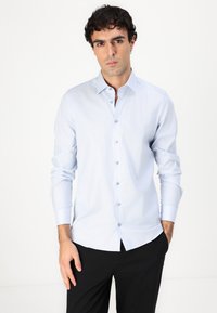 Chemise boutonnée bleu clair à manches longues, avec un motif texturé, un tissu doux et un col classique, associée à un pantalon noir.