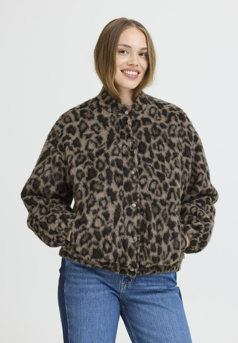 Veste en imprimé léopard en matériau doux et duveteux. Présente un col montant, une fermeture à boutons et deux poches latérales. Portée avec un jean bleu.