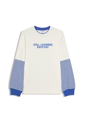 Weißes Langarmhemd mit blau gestreiften unteren Ärmeln und Manschetten, blauem Kragen und dem blauen Schriftzug „STILL LEARNING EACH DAY“ auf der Brust.