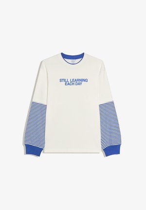 Valkoinen pitkähihainen paita, jossa siniset raidalliset hihansuut ja kalvosimet, sininen kaulus sekä sinisellä teksti "STILL LEARNING EACH DAY" rinnassa.