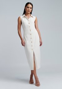Mouwloze linnen midi-jurk in lichtbeige, met een knopenrij aan de voorkant, kraag en een zijsplit, voorzien van grote neutrale knopen en een getailleerde pasvorm.