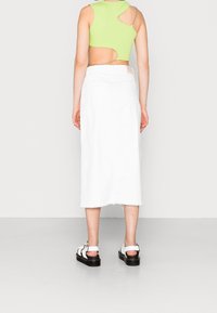 Jupe en denim blanc avec ourlet effiloché, associée à un crop top vert lime avec un design découpé et des détails en chaîne argentée. Sandales noires et blanches.