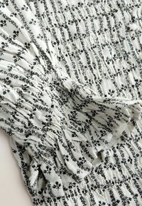Tissu blanc à petit motif floral noir et texture smockée élastique, rassemblée en plis ondulés.