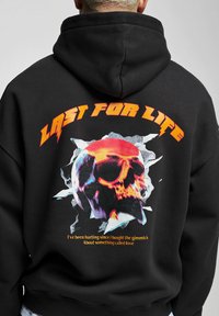 Black hoodie featuring a large, colorful skull graphic surrounded by jagged accents. Text reads "LAST FOR LIFE" in bold orange letters.