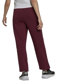 Burgundy sweatpants med avslappnad passform, tillverkade av mjukt tyg. Har en slät yta och rak ben-design, kombinerad med sportiga svarta sneakers.