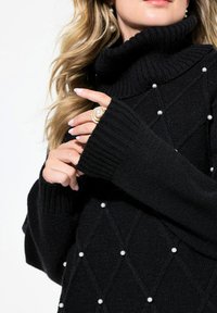 Schwarzer Rollkragenpullover mit geripptem Muster, Rautenmustern und Perlenverzierungen. Lange Ärmel mit verlängerten Bündchen.