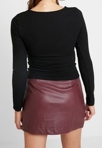 Musta ribattuvallis pitkähihaine paita yhdistettynä tiukkaan burgundinväriseen nahkaminihameeseen. Tekstuurit erottuvat selvästi, korostaen molempia vaatteita.