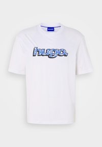 T-shirt blanc à col rond avec manches courtes, arborant le mot "HUGO" dans un design floral noir et bleu. Matière en coton doux, coupe décontractée.
