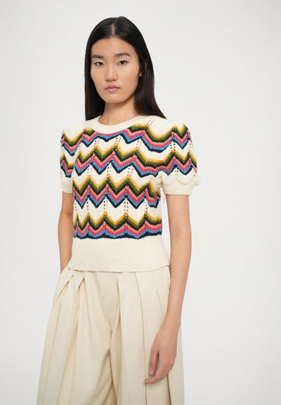 Pull en tricot à manches courtes avec un motif en zigzag en fil multicolore sur fond crème, présenté avec un ourlet côtelé et des manches bouffantes.