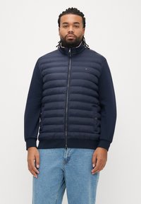 Laivastonsininen toppatakki tikatulla kuviolla, korkealla kauluksella, kokopitkällä vetoketjulla ja resorinauhatuilla hihoilla. Sopii hyvin yhdistettäväksi yksiväriseen siniseen kangasrunkoon hihoissa ja sivuilla.