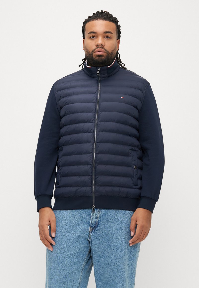 Laivastonsininen toppatakki tikatulla kuviolla, korkealla kauluksella, kokopitkällä vetoketjulla ja resorinauhatuilla hihoilla. Sopii hyvin yhdistettäväksi yksiväriseen siniseen kangasrunkoon hihoissa ja sivuilla.