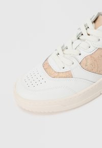 Zapatilla blanca con paneles de encaje beige texturizados, punta perforada para transpirabilidad y cordones blancos. Suela de goma de color claro.